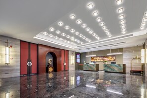 Un moderno vestíbulo con piso de mármol, una mesa de recepción y una pantalla digital que muestra información.