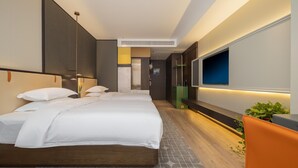 Una habitación de hotel moderna con una cama grande, un televisor montado en la pared y un pequeño rincón de estar con una planta.