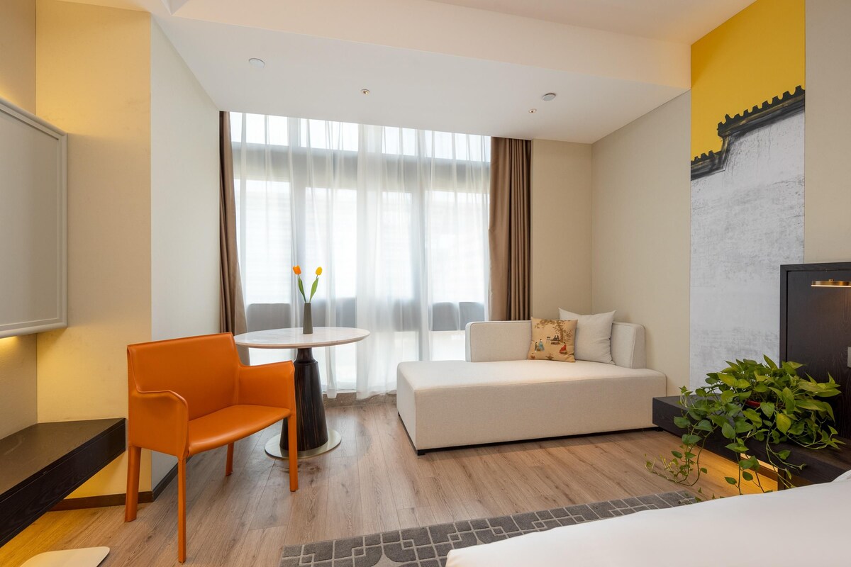 Une chambre d’hôtel avec un canapé, une table à manger avec des chaises, un téléviseur et une plante.