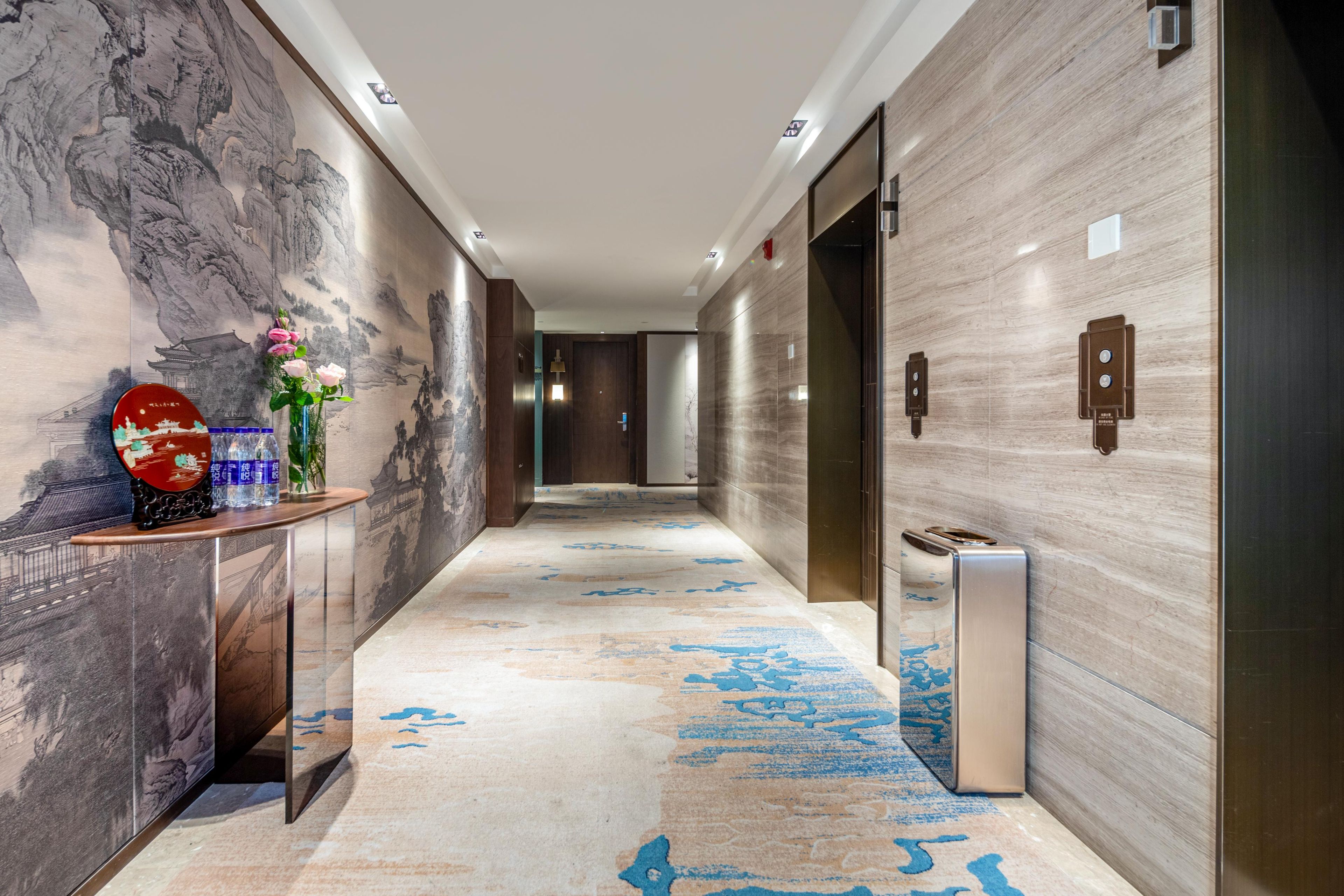 A modern hallway with a marble floor, a reception desk with a vase of flowers, and a wall with a traditional painting.
