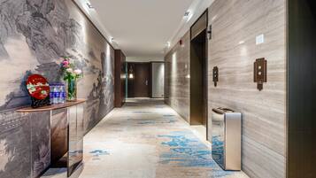 A modern hallway with a marble floor, a reception desk with a vase of flowers, and a wall with a traditional painting.
