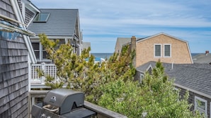 A residential area with a view of the ocean, a wooden house, and a grill on a deck.