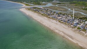 An aerial view of a coastal residential area with houses along the shoreline, a sandy beach, and a river or bay with water channels.