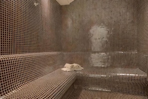 A tiled room with a bench, a towel, and a mirror. - Hotel Morione & Spa Center (Istanbul)
