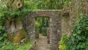 A stone archway leading to a pathway surrounded by greenery and moss-covered walls. - Coach House, Holiday Cottage Stackpole , Sleeps 8, 4 bedrooms,  bathrooms (Pembroke)