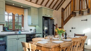 A rustic kitchen with a wooden table set for dining, a refrigerator, and a sink. - Coach House, Holiday Cottage Stackpole , Sleeps 8, 4 bedrooms,  bathrooms (Pembroke)