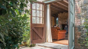 A rustic stone building with a wooden door and steps leading to a cozy interior featuring a fireplace and a patterned sofa. - Coach House, Holiday Cottage Stackpole , Sleeps 8, 4 bedrooms,  bathrooms (Pembroke)