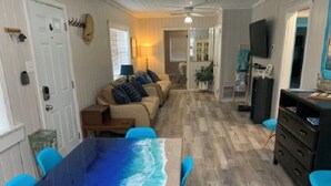 En matplats med ett bord som har ett blått havsmotiv, en soffa med kuddar, en tv och en byrå.