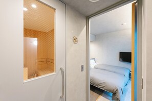 A hotel room with a wooden shower enclosure, a bed with grey bedding, and a mounted TV on the wall.