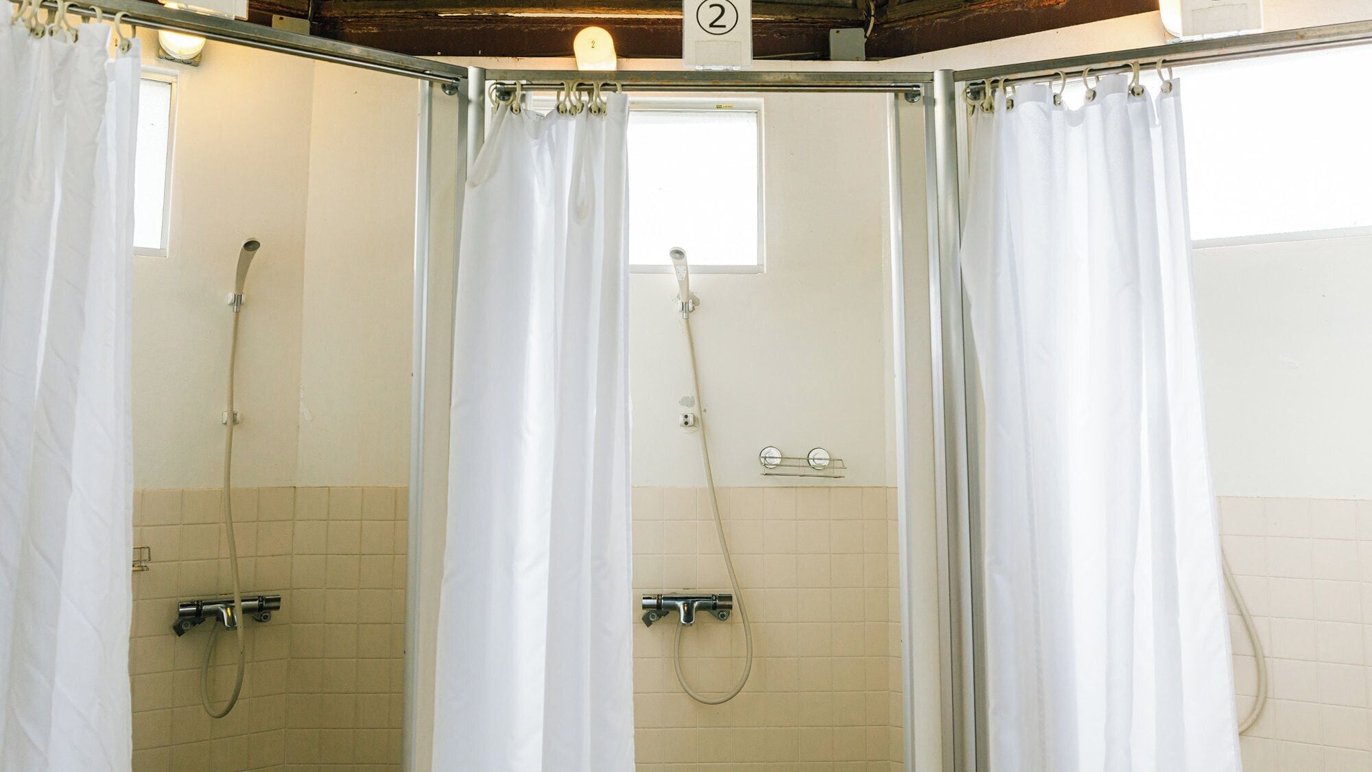 A shower area with white curtains, a window, and tiled walls.