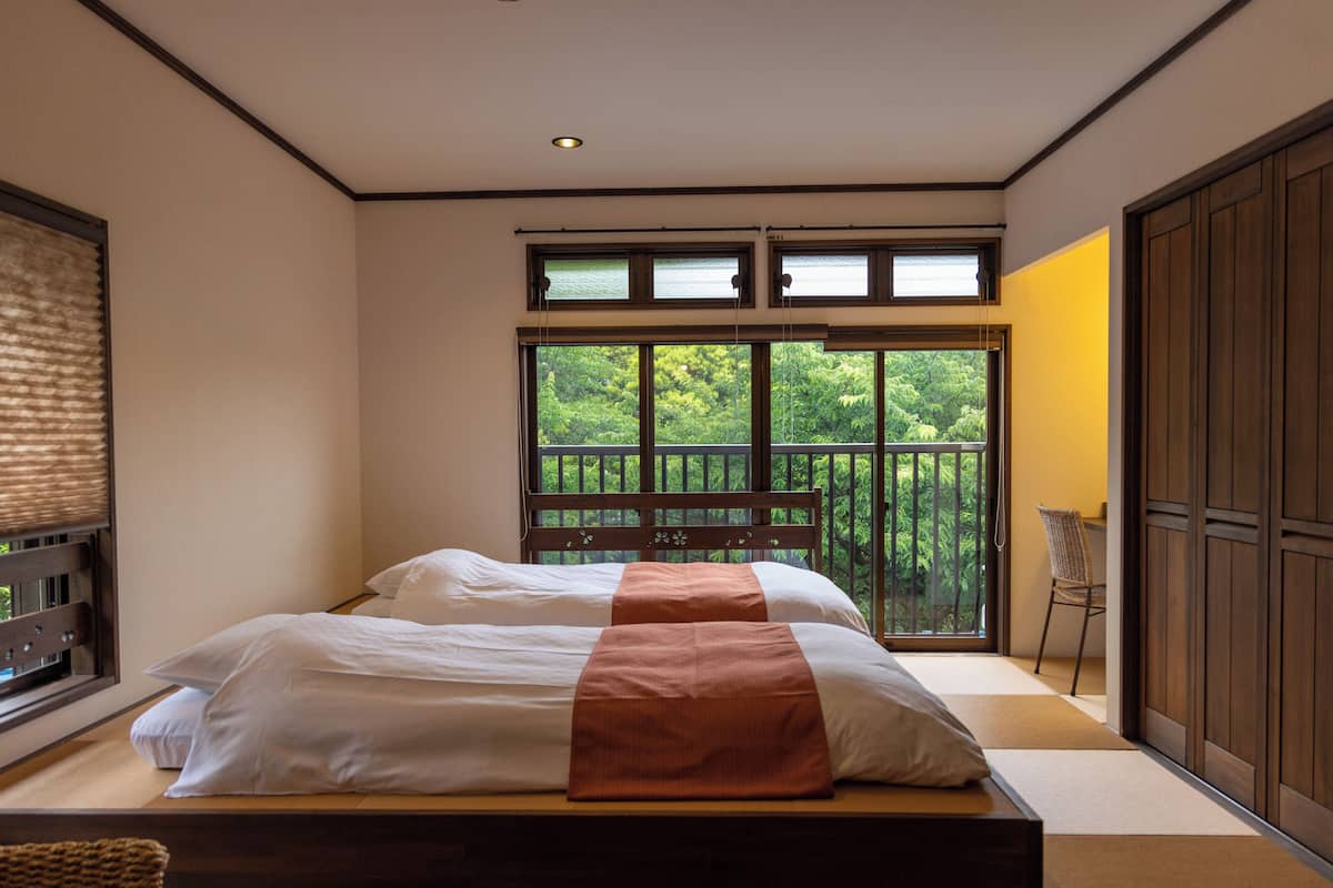 A bedroom with a large bed, a view of greenery through a sliding door, and a wooden wardrobe.