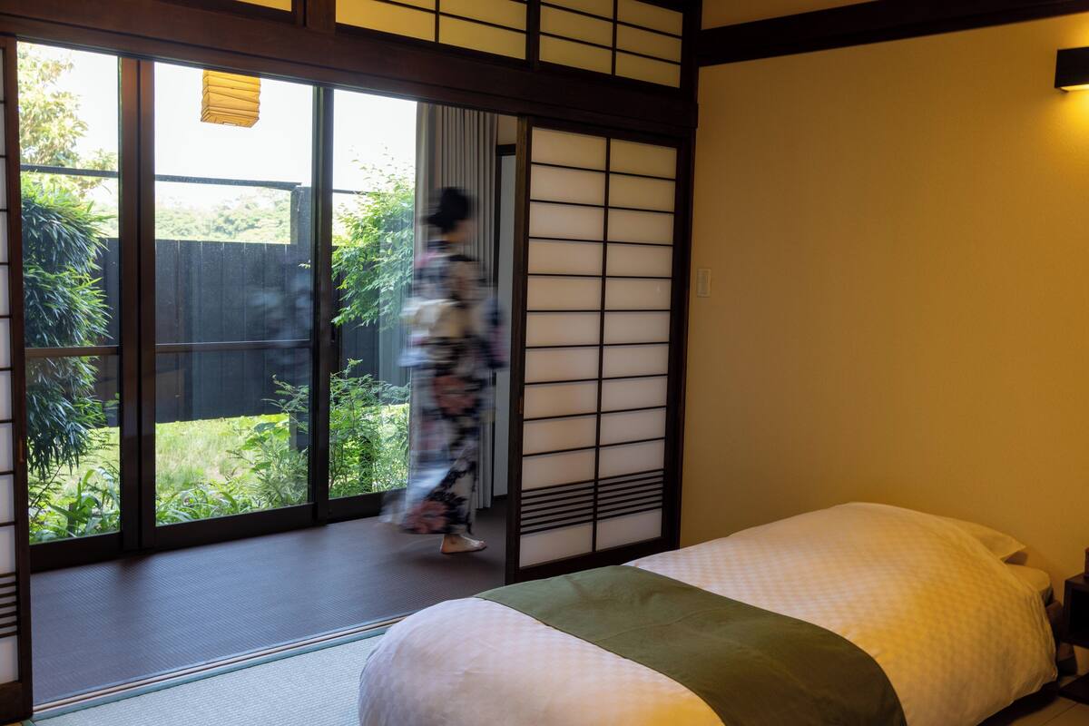A traditional Japanese room with tatami flooring, a sliding door leading to a garden, and a bed with a green and white bedding.