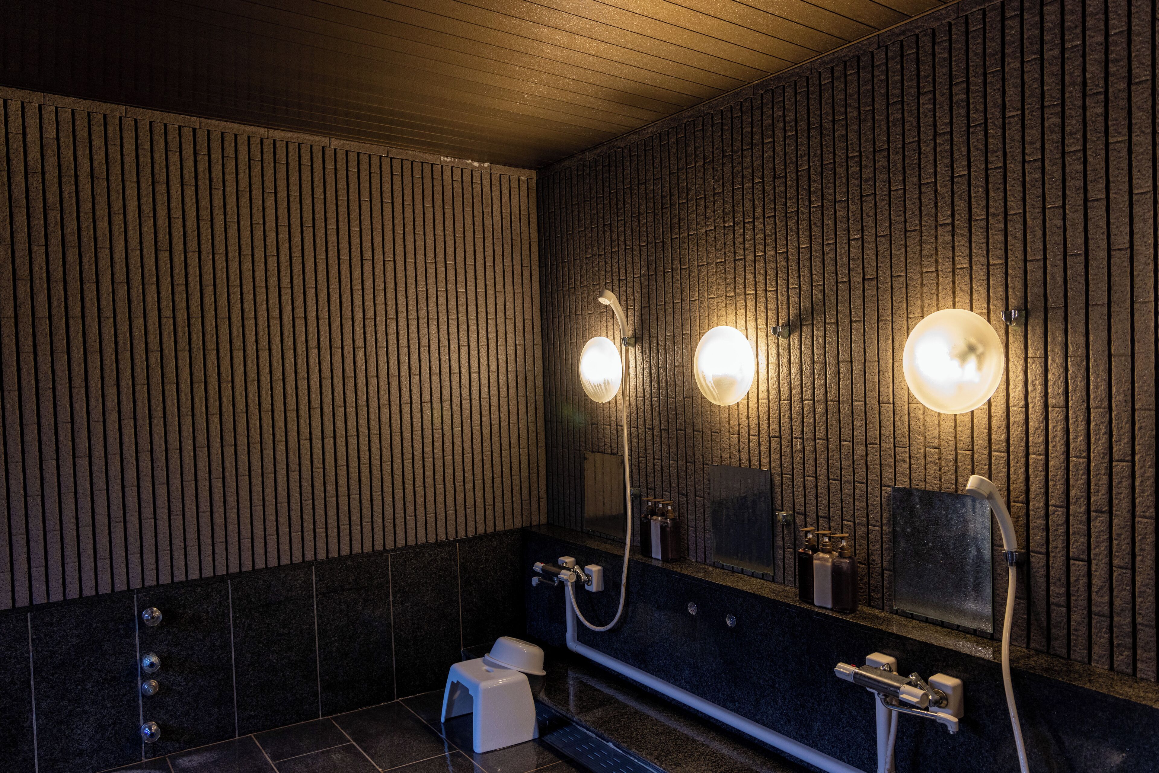 A modern bathroom with a wooden slat wall, a large mirror, and a handheld showerhead.