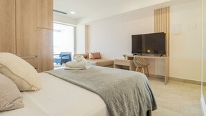 A modern hotel room with a bed, a desk with a TV, a chair, and a view of the outdoors. - Panoramic Oceanview Loft Near Beach & Airport (Cartagena de Indias)