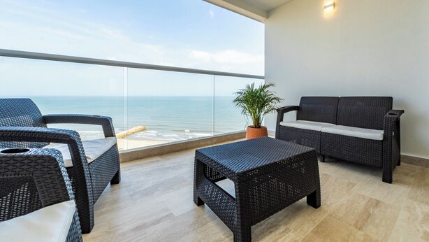 A balcony with wicker furniture, a potted plant, and a view of the ocean. - Panoramic Oceanview Loft Near Beach & Airport (Cartagena de Indias)