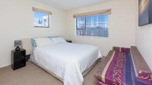 A bedroom with a bed, a nightstand, a lamp, a window with curtains, and a view of the outside.