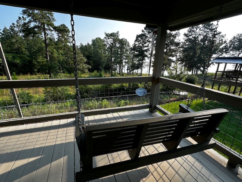 A wooden deck with a swing, a metal fence, and a view of trees.