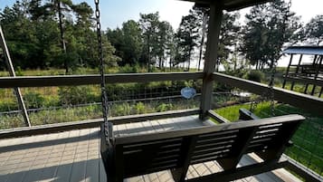 A wooden deck with a swing, a metal fence, and a view of trees.