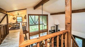 A wooden staircase leading to a deck with a view of greenery. A dining area with a table and chairs is visible in the background.