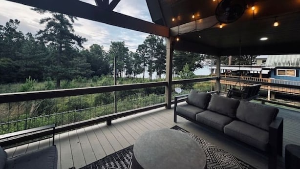 A covered outdoor deck with a sofa and a round table, overlooking a natural landscape.