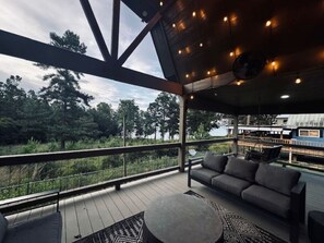 Eine überdachte Terrasse im Freien mit einer Couch und einem runden Tisch, mit Blick auf eine natürliche Landschaft.