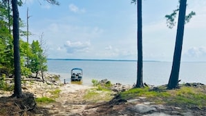 A beach with a vehicle parked on the sand, surrounded by trees and a body of water in the background.