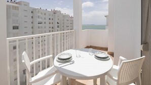 A balcony with a white table set for two, overlooking a body of water and buildings.