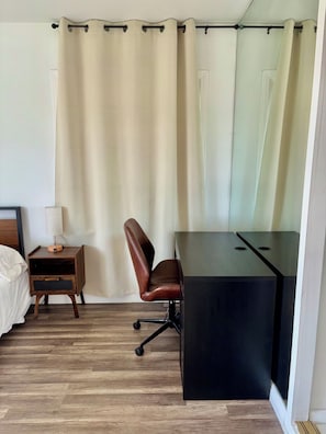 Et hotelværelse med trægulv, et skrivebord med stol, et sengebord med lampe og en seng.