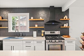 A modern kitchen with a black hexagonal backsplash, white cabinetry, a stainless steel stove, and wooden shelves.