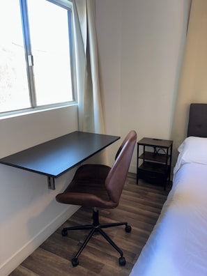 Et værelse med skrivebord, stol, seng og natbord.