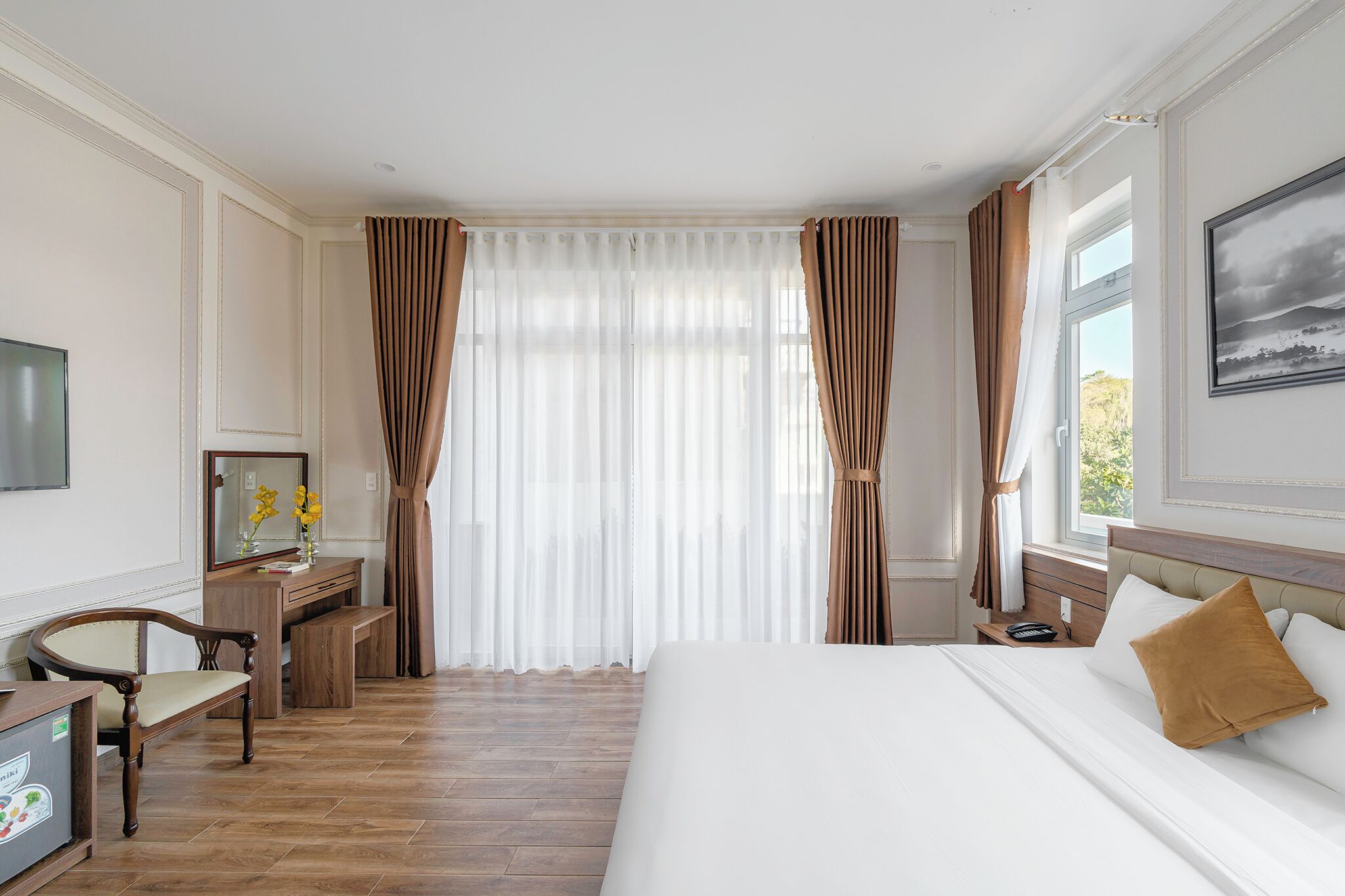 A hotel room with a bed, a desk, a chair, a TV, and a window with curtains.