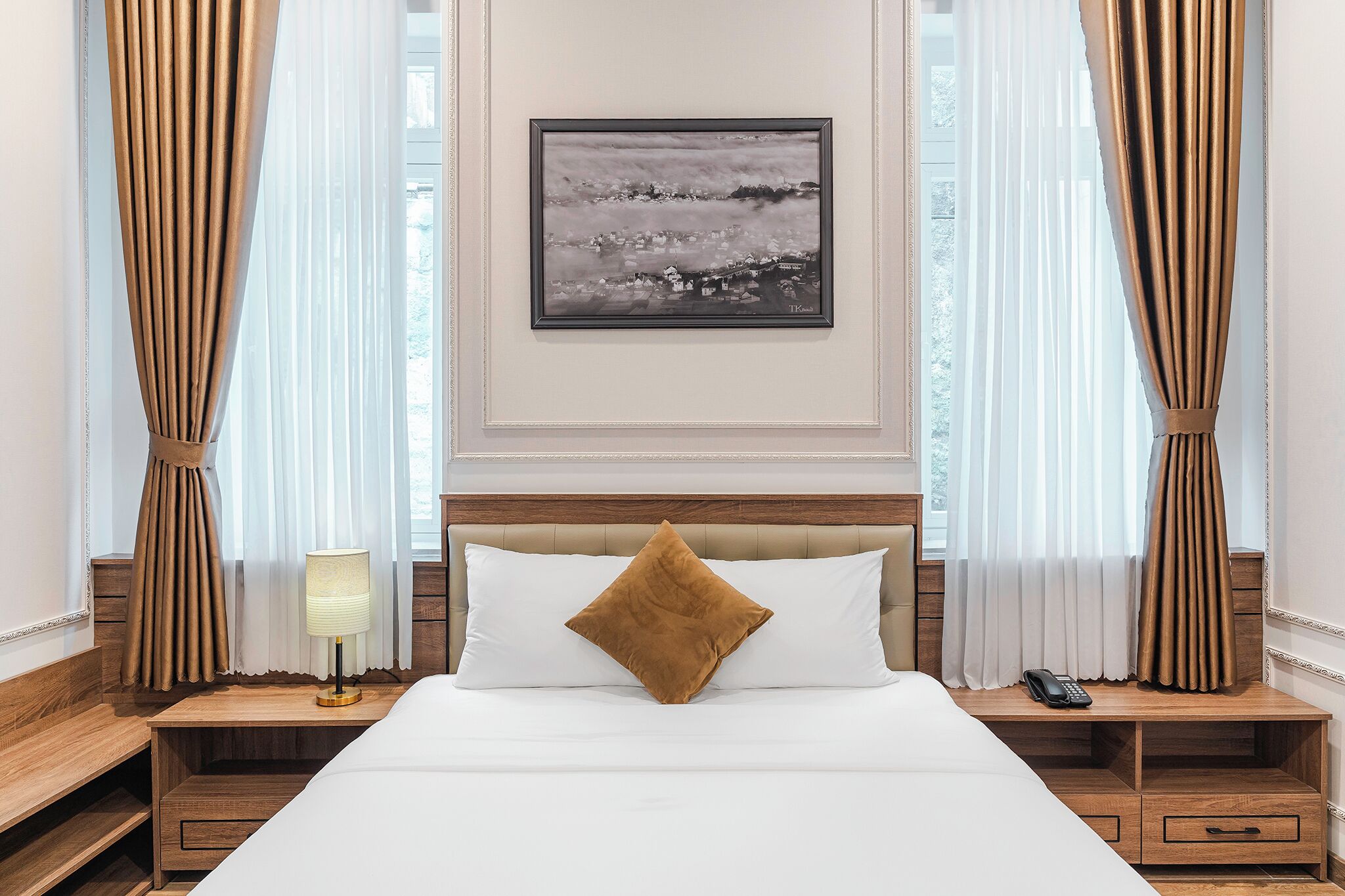 Una habitación de hotel con cama, mesita de noche con lámpara, cuadro enmarcado en la pared y cortinas.