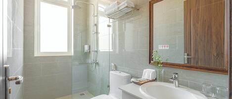 A modern bathroom with a glass shower enclosure, a toilet, a sink with a mirror, and a window providing natural light.