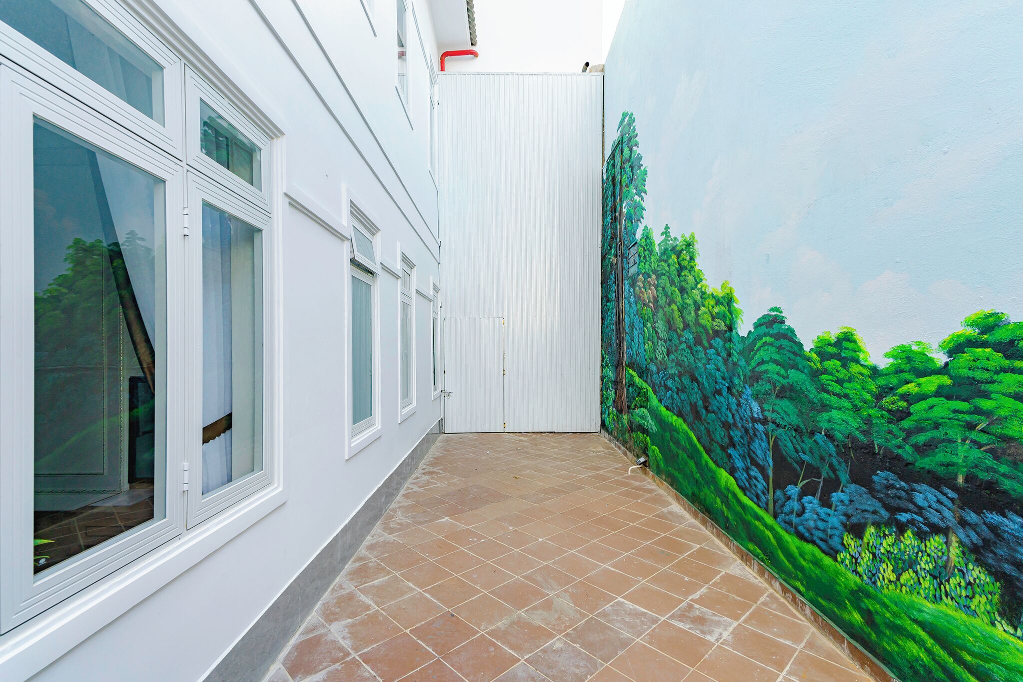 Un pasillo con suelo de baldosas, paredes blancas y un mural que representa un paisaje boscoso.