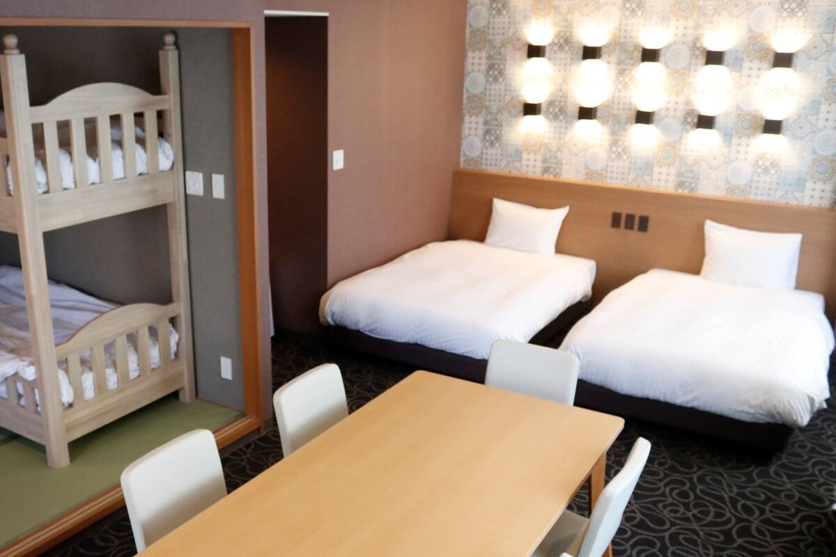 A hotel room with bunk beds, a single bed, a table, chairs, and a patterned wall.