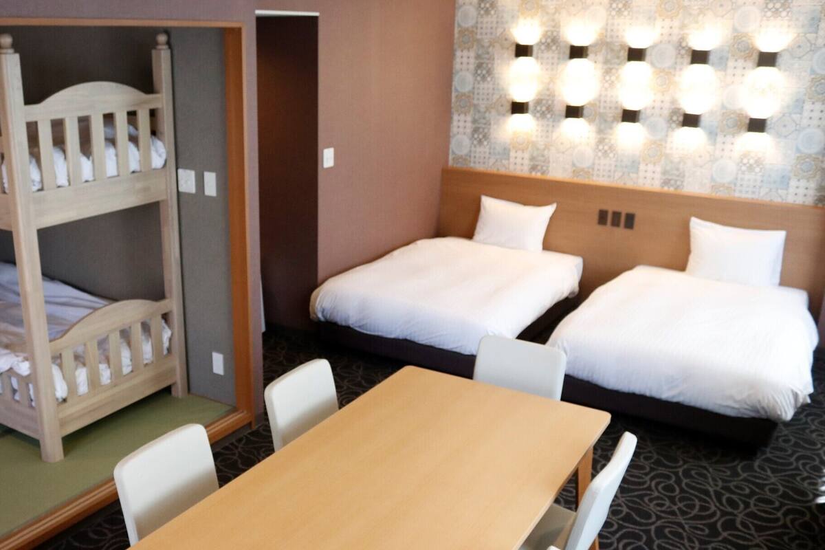 A hotel room with bunk beds, a single bed, a table, chairs, and a patterned wall with lights.