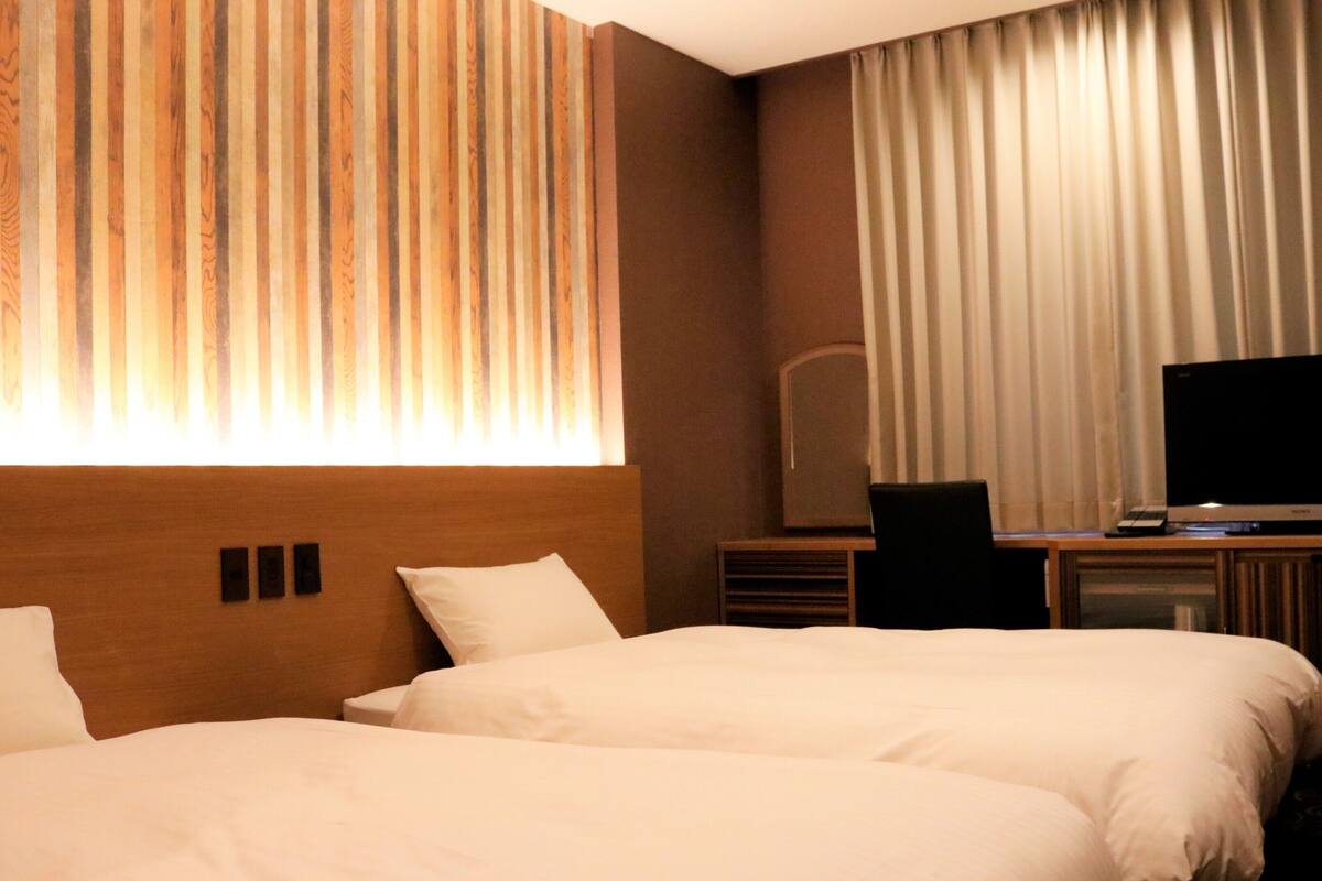 A hotel room with two beds, a television, and a desk with a computer.