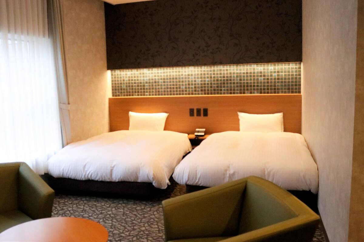 A hotel room with two beds, a small table, and two armchairs.