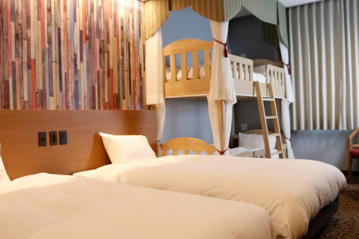 A hotel room with a bunk bed, a wooden headboard, a bedside table, and a chair.