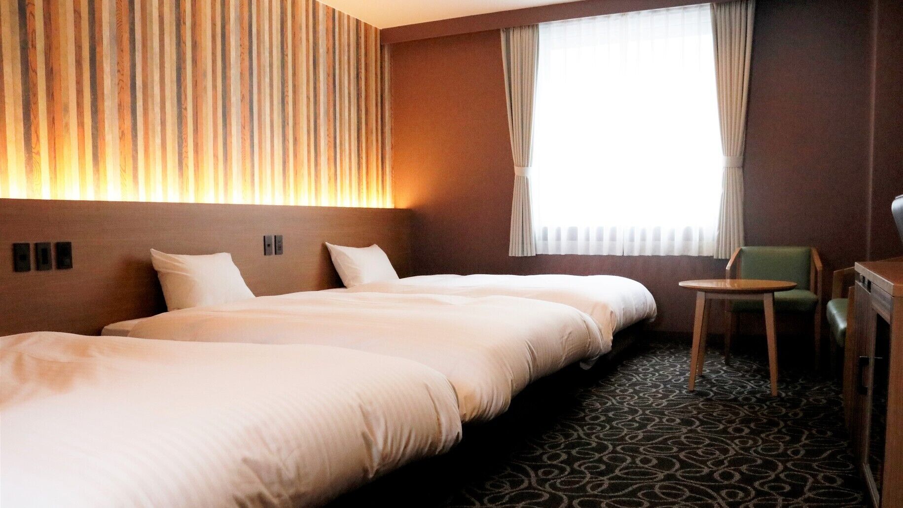 A hotel room with three beds, a small table, and a chair.