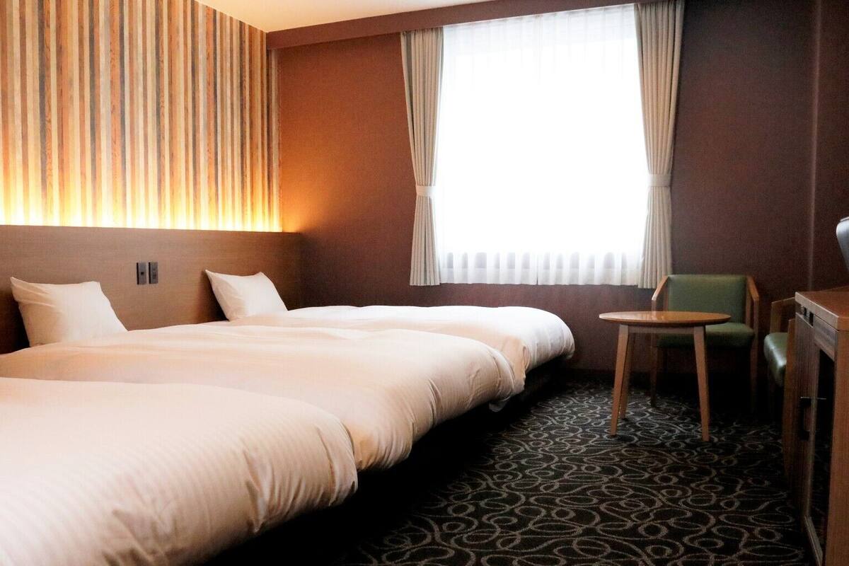 A hotel room with three beds, a small table, and a chair.