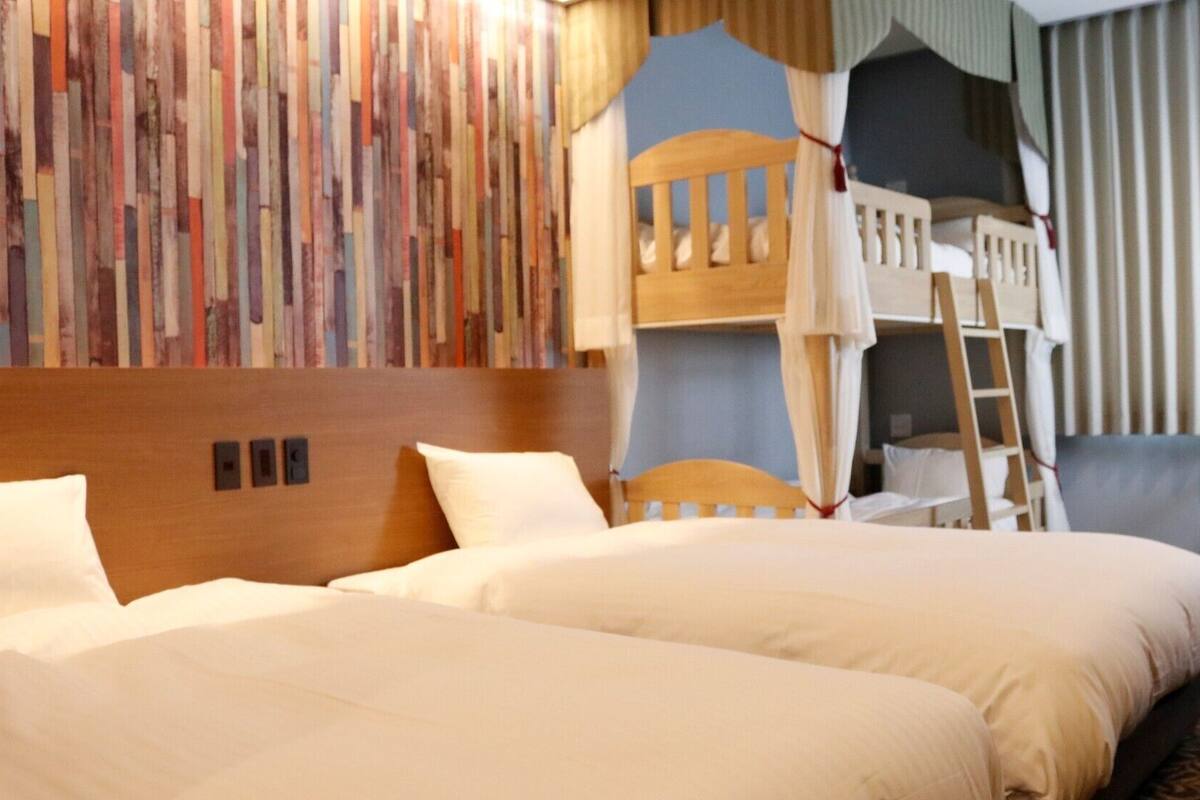 A hotel room with two beds, a bunk bed, a wooden headboard, a red chair, and a patterned wall.