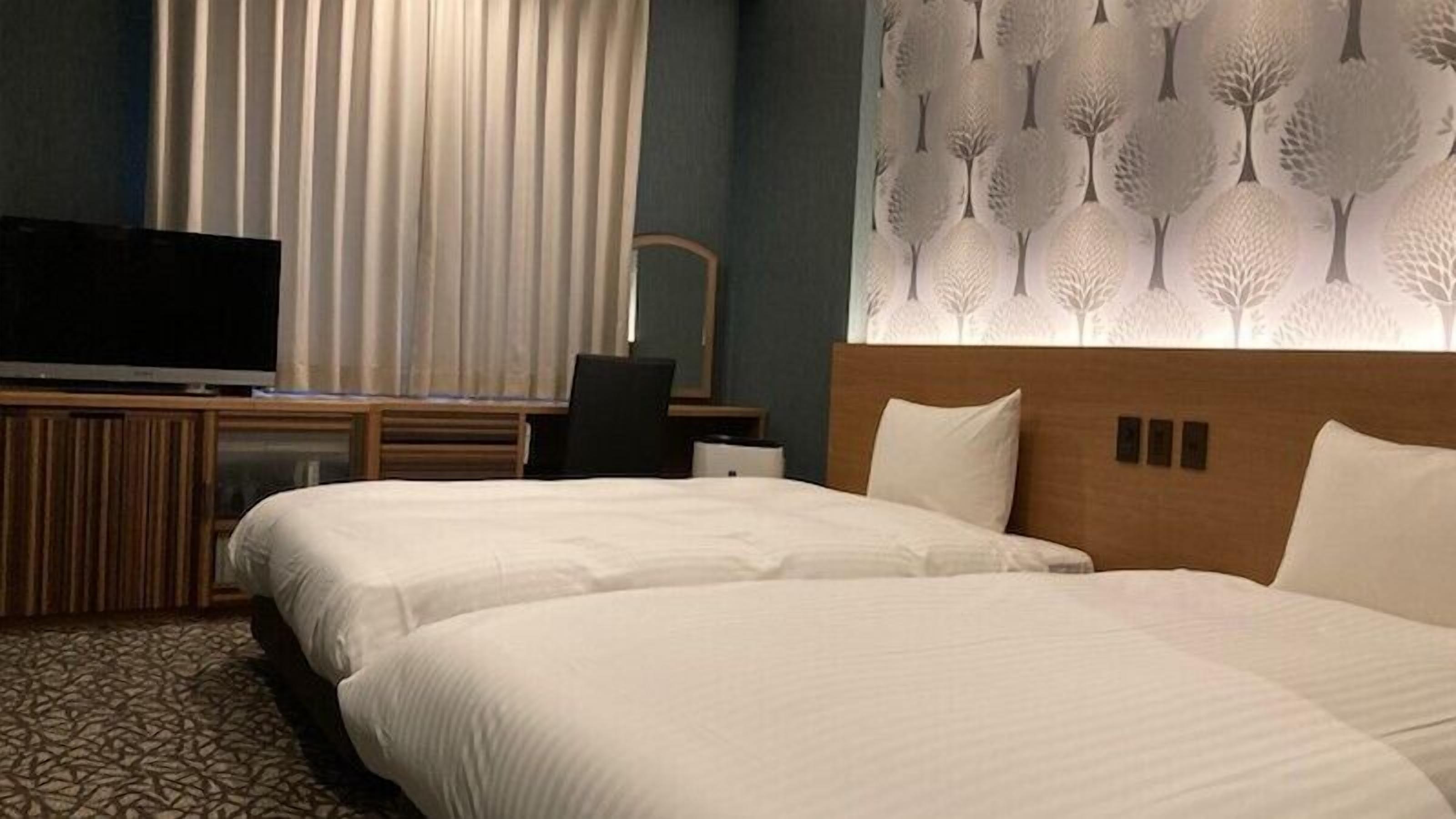 A hotel room with two beds, a TV, a desk, and a wall with a tree pattern.