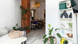 A modern living room with a brick accent wall, a dining area with a wooden table and chairs, and a white bookshelf with decorative items. - Cozy Apartment 810 Matamoros (Puerto Vallarta)