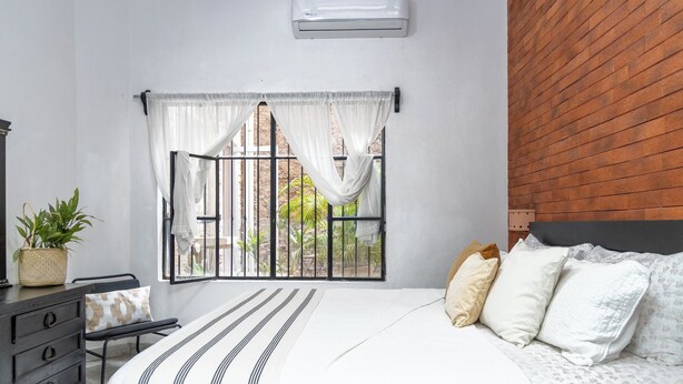 A bedroom with a bed, a dresser, a potted plant, and a window with curtains. - Cozy Apartment 810 Matamoros (Puerto Vallarta)