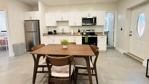 A modern kitchen with white cabinets, stainless steel appliances, and a wooden dining table with chairs. - Cute & Spacious 2BR/2Bath Home in FLL w/ Patio (Fort Lauderdale)