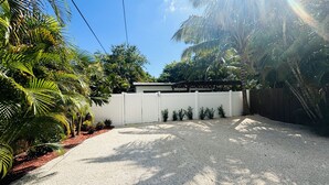 A gravel driveway leading to a white gate, surrounded by lush greenery and palm trees. - Cute & Spacious 2BR/2Bath Home in FLL w/ Patio (Fort Lauderdale)