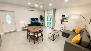 A modern living room with a dining area, a gray sofa with yellow cushions, a TV, and a ceiling fan. - Cute & Spacious 2BR/2Bath Home in FLL w/ Patio (Fort Lauderdale)