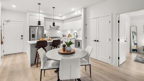 A modern kitchen with white cabinetry, a central island, and a dining area with a round table and chairs. - Luxury White Rock 2BR | King Bed | Sleeps 6| Parking (Surrey)