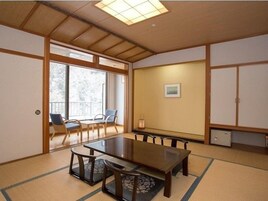 Una habitación tradicional japonesa con suelo de tatami, una mesa baja con cojines y puertas correderas.